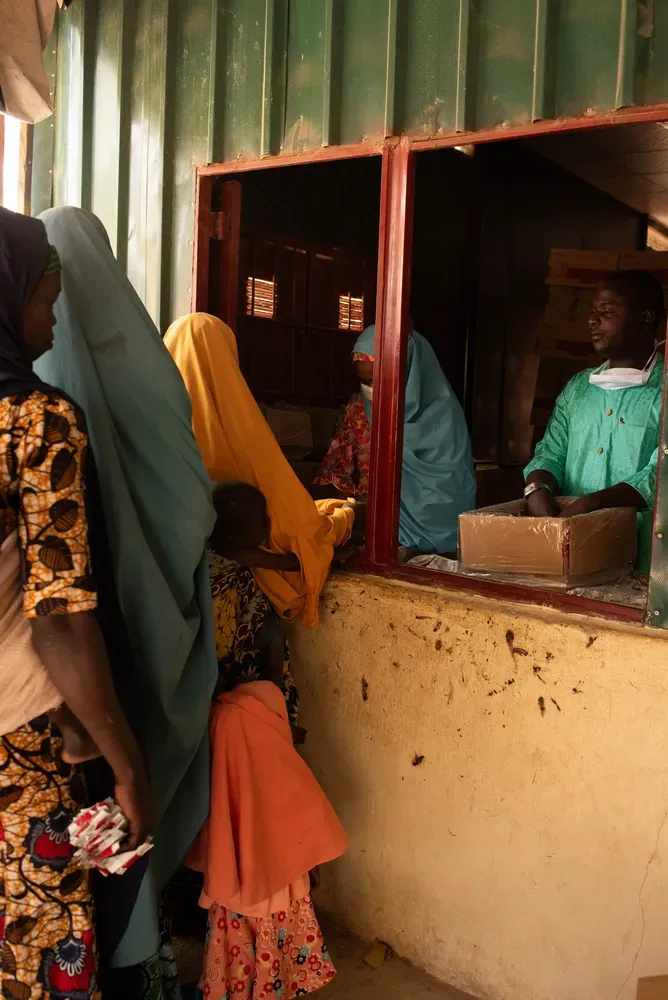 نساء يرتدين ملابس تقليدية يتلقين الأدوية من موظف في نقطة توزيع، في سياق جهود مكافحة الملاريا في جمهورية الكونغو الديمقراطية.