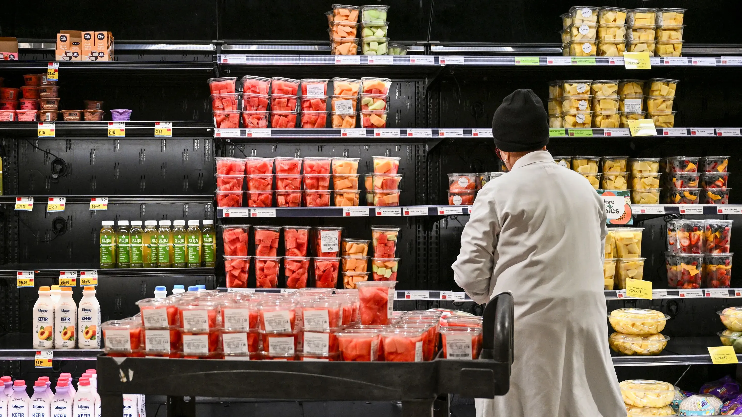 متسوق في متجر بقالة يتفقد رفوف الفواكه المعبأة، حيث تظهر أسعار المواد الغذائية المرتفعة وسط تراجع التضخم.