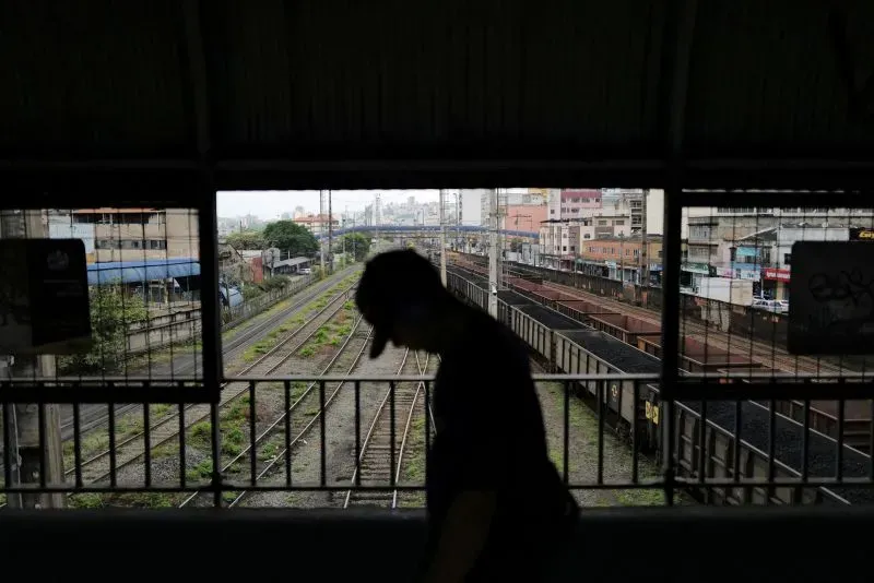 مشهد لراكب يسير في محطة قطار، مع خطوط السكك الحديدية والمباني في الخلفية، يعكس حركة النقل في البرازيل وسط التوترات التجارية.