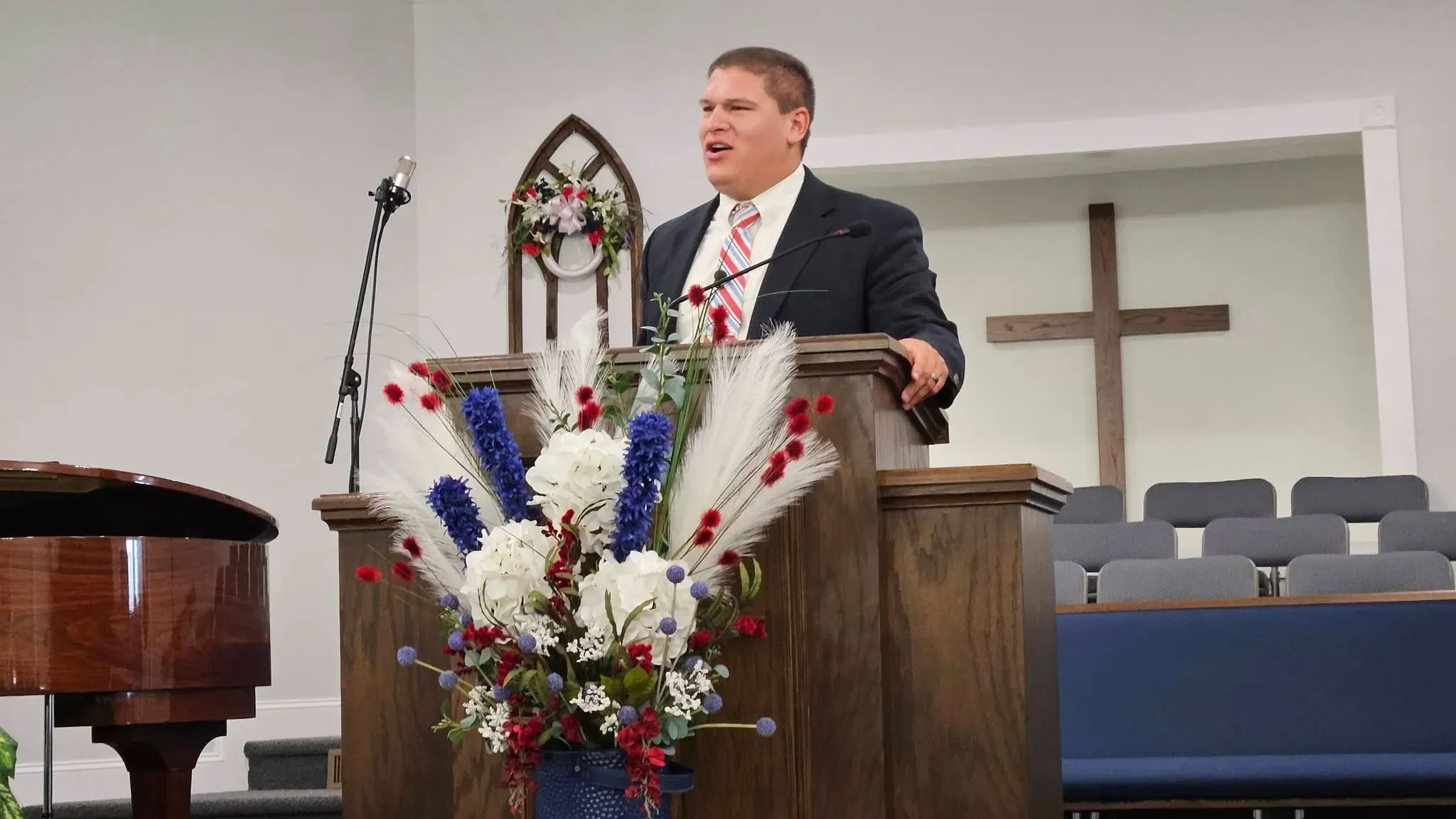 واعظ أمريكي يلقي خطبة في كنيسة، مع زهور ملونة وزينة خلفه، في سياق حديث عن عملية إنقاذه من الاختطاف في جنوب أفريقيا.