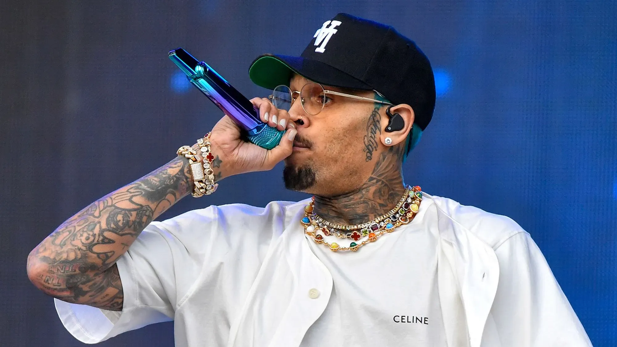 المغني الأمريكي كريس براون يؤدي على المسرح، مرتديًا نظارات وقبعة، مع ميكروفون ملون في يده، وسط أضواء ساطعة.