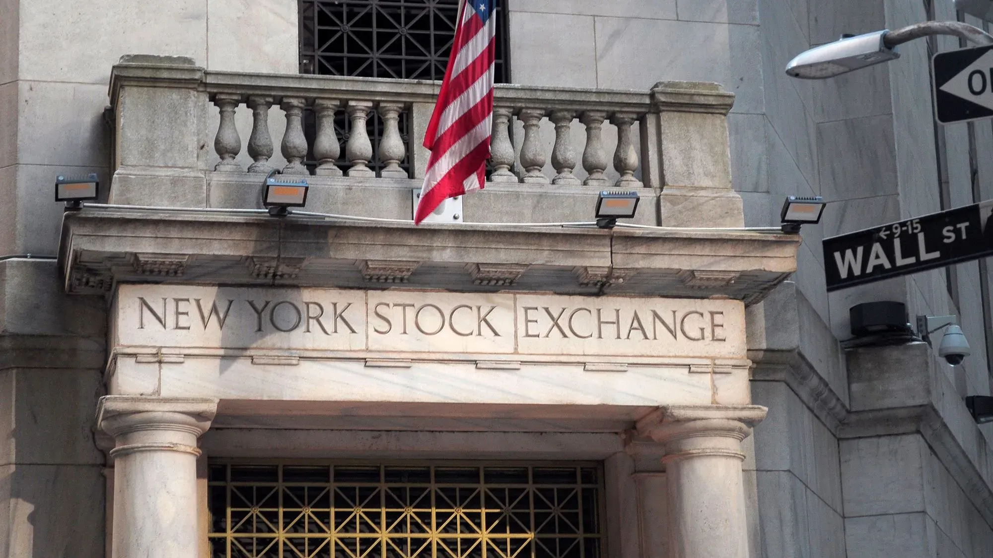 واجهة بورصة نيويورك مع العلم الأمريكي، تعكس التوترات الاقتصادية بعد فرض رسوم جمركية جديدة على السلع.