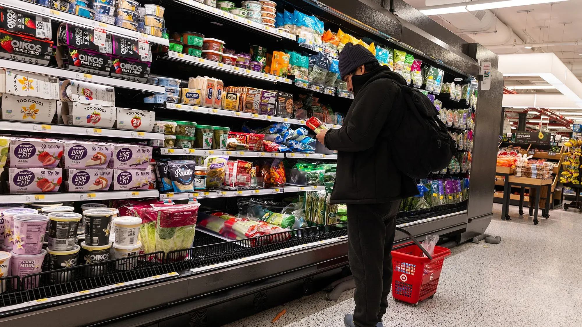 شخص يتسوق في متجر، يركز على اختيار المواد الغذائية من الرفوف، مع تواجد مجموعة متنوعة من المنتجات.