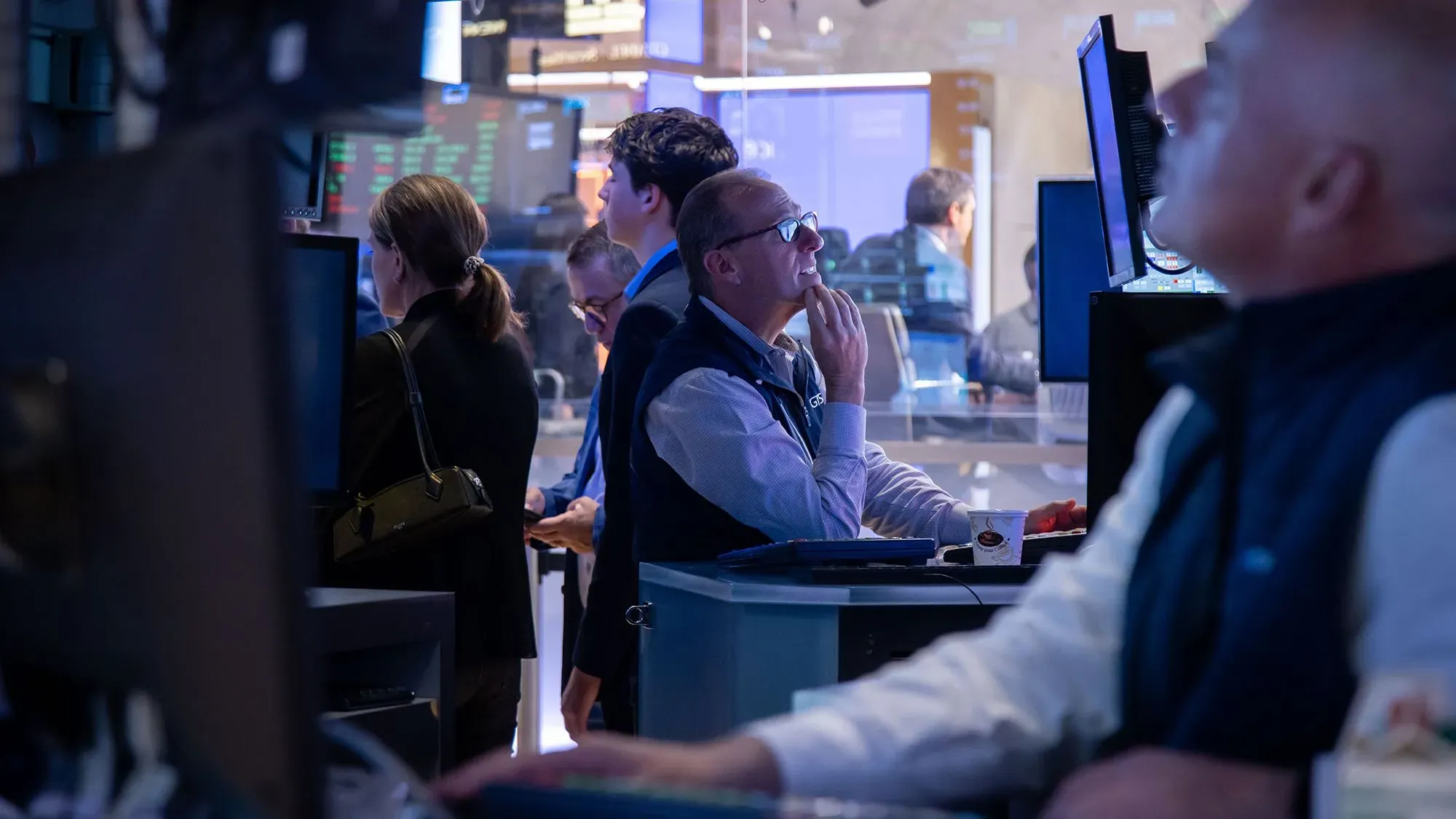 تظهر الصورة مجموعة من المتداولين في بورصة وول ستريت، يراقبون شاشات الأسهم في أجواء من القلق بسبب تراجع الأسواق.