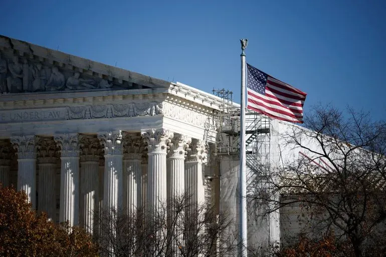 واجهة المحكمة العليا الأمريكية مع أعمدة بارزة وعلم الولايات المتحدة يرفرف في الهواء، تعكس الجدل حول إعادة رسم الدوائر الانتخابية.