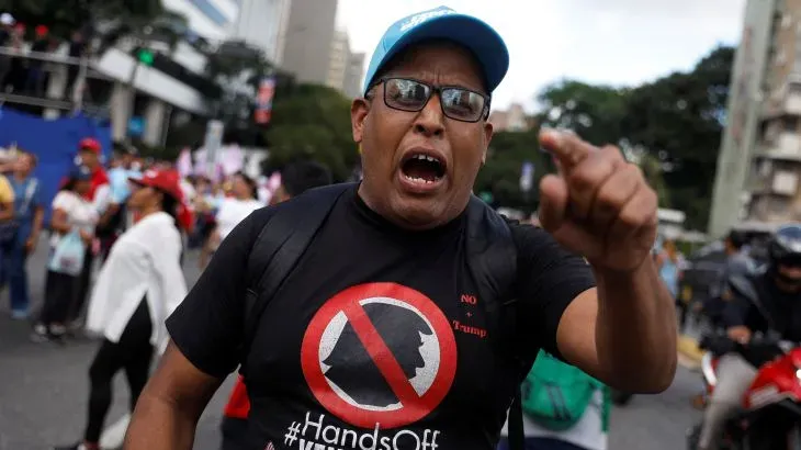 رجل في مظاهرة بفنزويلا يرتدي قميصًا يعبّر عن معارضته لتدخل الولايات المتحدة، بينما يعبر عن مشاعره بحماس.