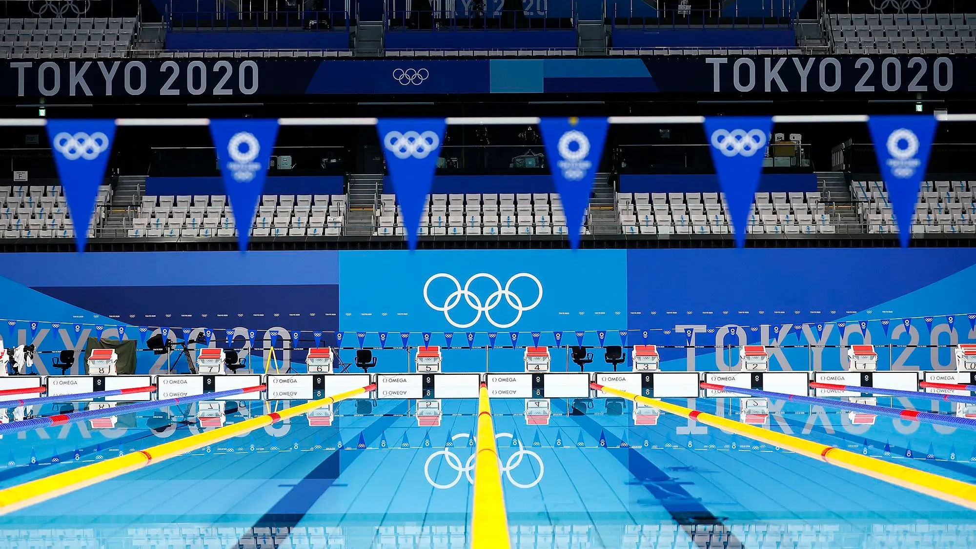 حمام السباحة الأولمبي في طوكيو 2020، مع علم الأولمبياد وأعلام زرقاء، يمثل موقع المنافسات وسط جدل حول قضايا المنشطات.