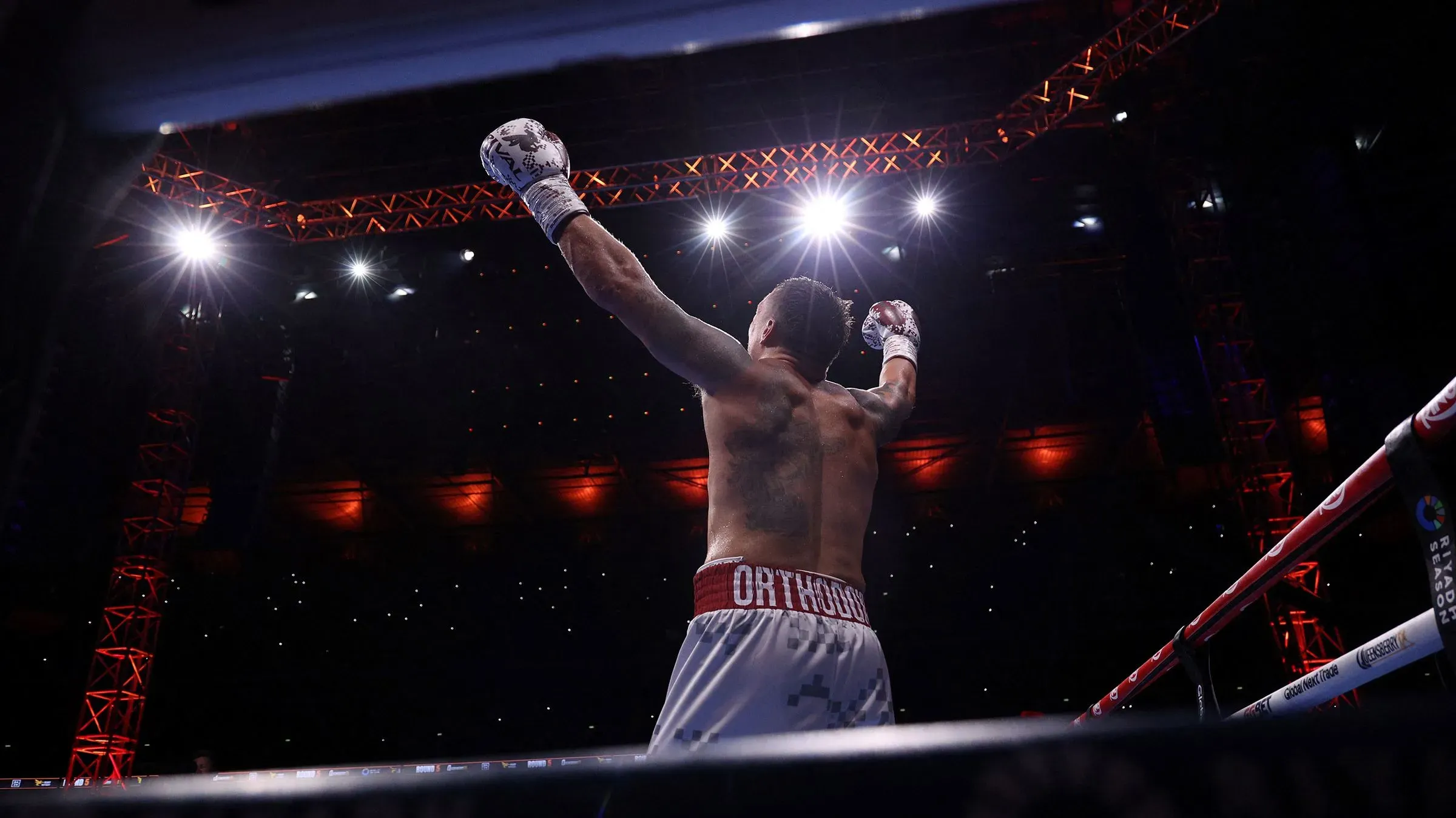 أوسيك يحتفل بفوزه بالضربة القاضية على دوبوا في نزال الوزن الثقيل، مع أضواء الملعب الساطعة وخلفية الجماهير في ويمبلي.
