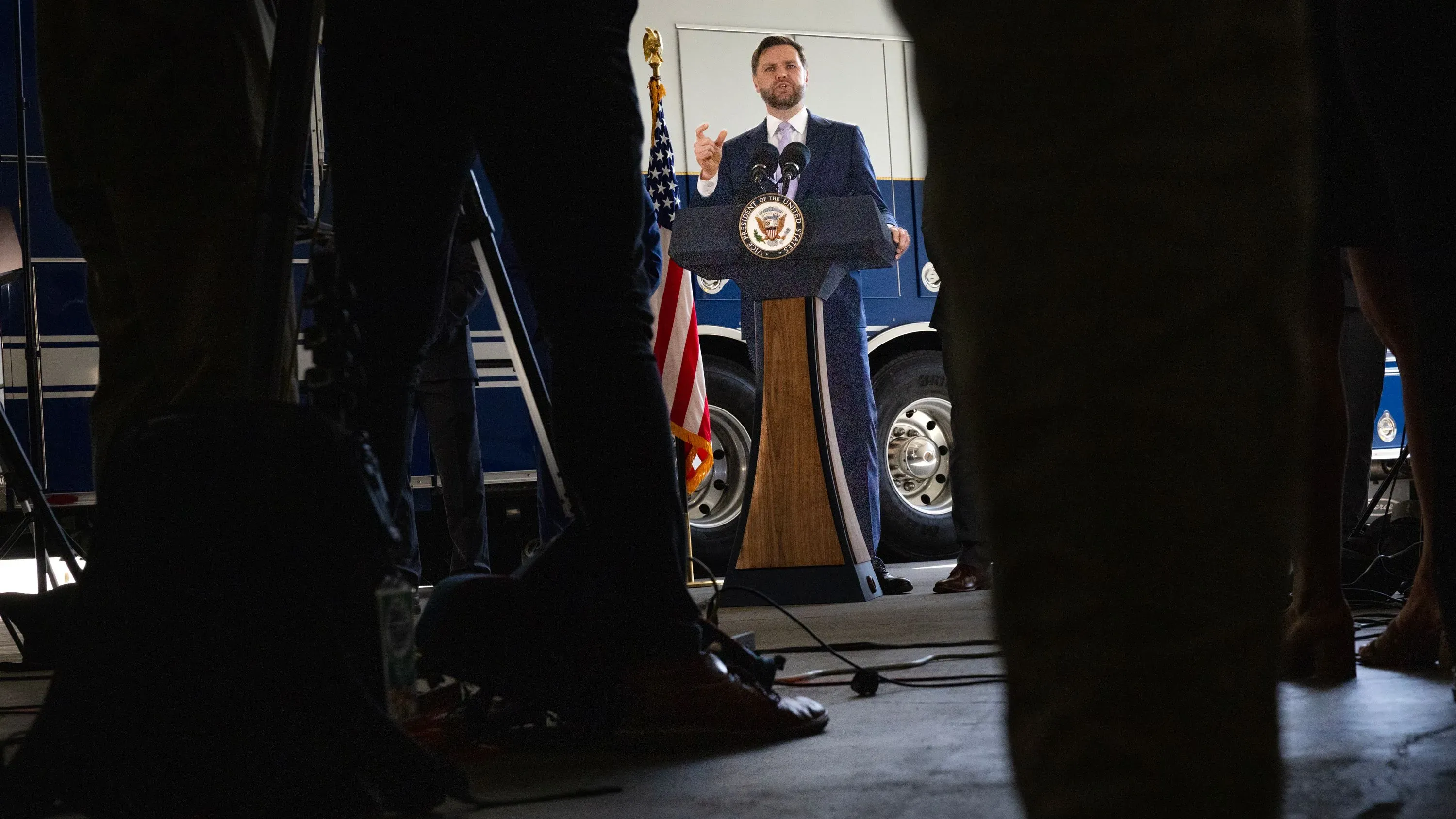 نائب الرئيس جيه دي فانس يتحدث من منصة خلال مؤتمر صحفي في لوس أنجلوس، محاطًا بالصحفيين، مع العلم الأمريكي خلفه.