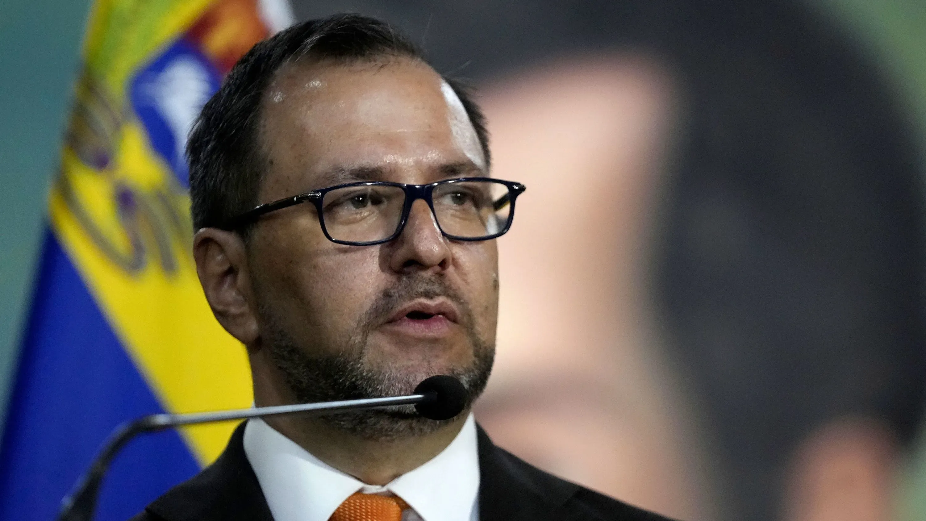 وزير الخارجية الفنزويلي إيفان جيل يتحدث في مؤتمر صحفي، مع العلم الفنزويلي خلفه، متناولًا أعمال التخريب ضد المنشآت الدبلوماسية.