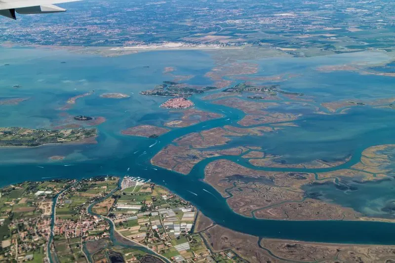 منظر جوي لمدينة البندقية والمناطق المحيطة بها، يظهر القنوات المائية والأراضي الزراعية، مع التركيز على التحديات البيئية التي تواجه المدينة.