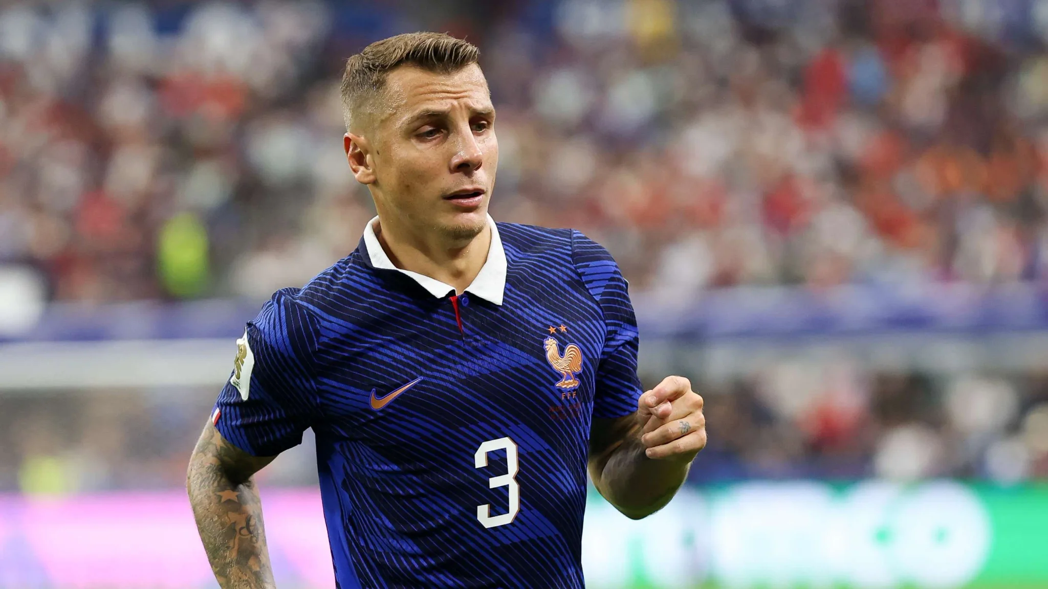 لوكاس ديغني لاعب كرة قدم فرنسي يرتدي قميص منتخب فرنسا رقم 3 خلال مباراة دولية، مع تركيز على عودته إلى باريس سان جيرمان.