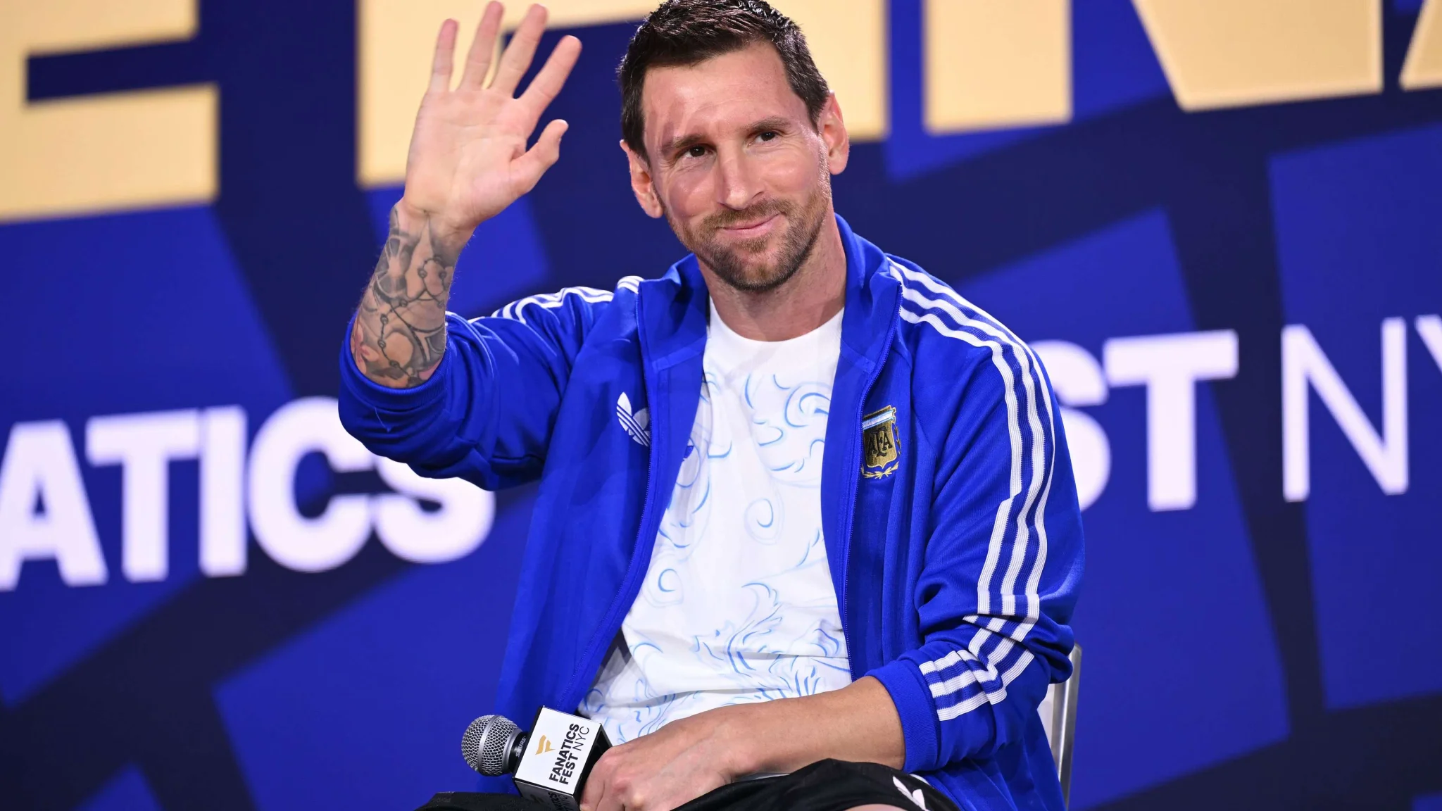 ليونيل ميسي يلوح بيده خلال مؤتمر صحفي على هامش كأس العالم، مرتدياً زي الأرجنتين الرياضي الأزرق.