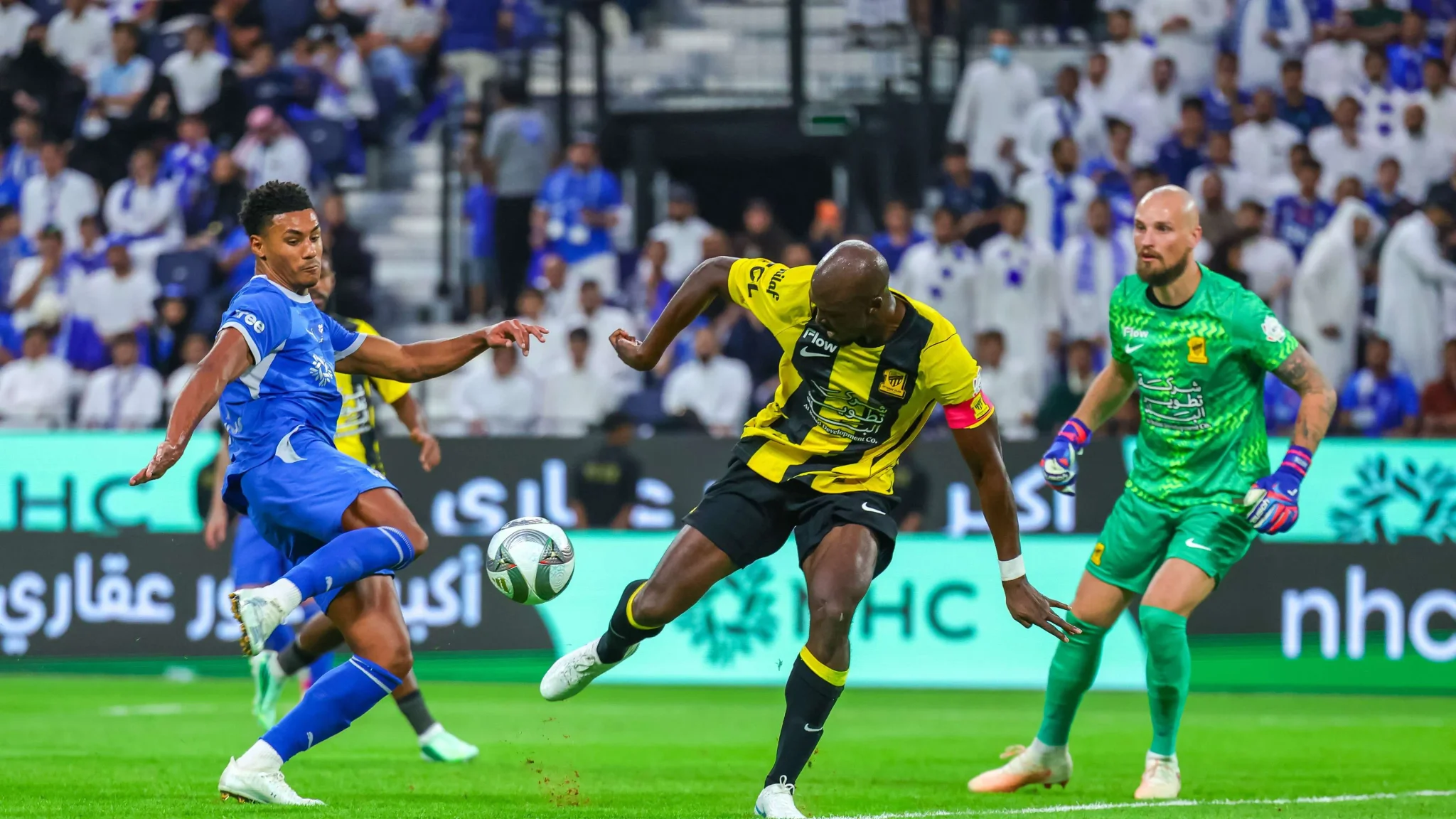 لاعبو الهلال والاتحاد يتنافسون على الكرة في مباراة دوري روشن السعودي، مع حارس الاتحاد مستعد للتصدي.