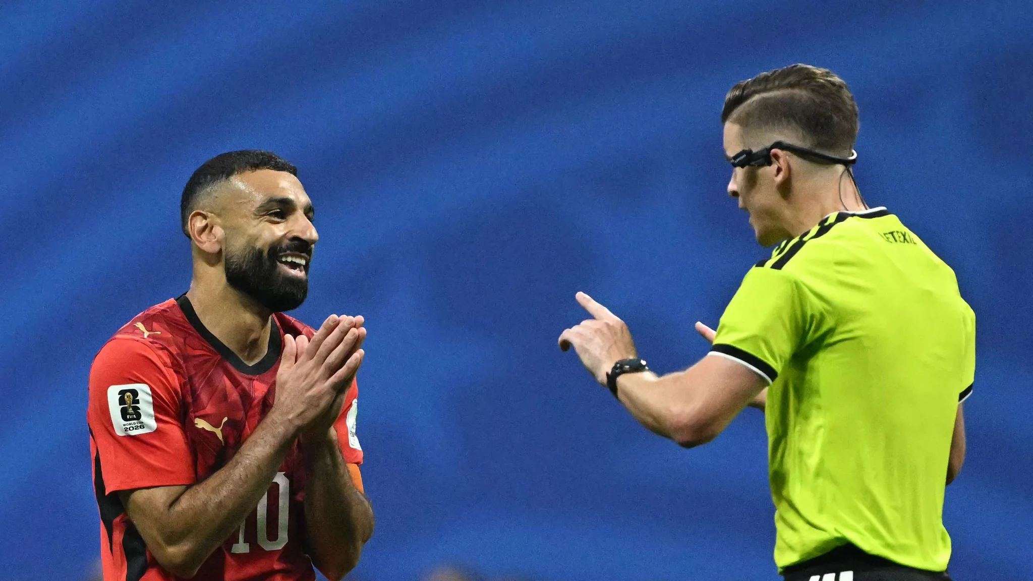 لاعب كرة قدم مصري يرتدي الرقم 10 يتحدث مع حكم المباراة خلال مواجهة مثيرة في كأس العالم، تعكس توتّر اللقاء وأداء الفراعنة المميز.