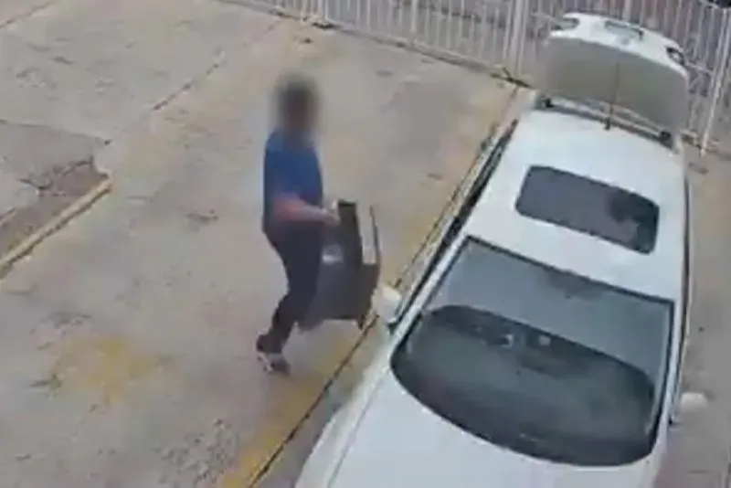 رجل يرتدي قميصًا أزرق يحمل حقيبة ثقيلة بالقرب من سيارة بيضاء، بينما يُظهر الفيديو جزءًا من التحقيق في مقتل لورينا موراليس.