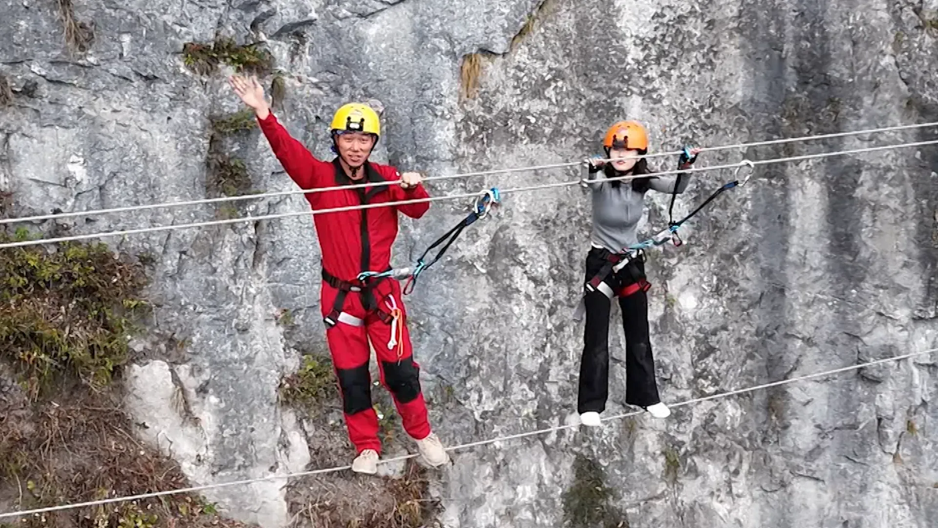 شخصان يرتديان خوذات واقية، يتسلقان حبلًا في متنزه غابة تشانغجياجيه، مع خلفية صخرية، مما يعكس مغامرات الطبيعة في المنطقة.