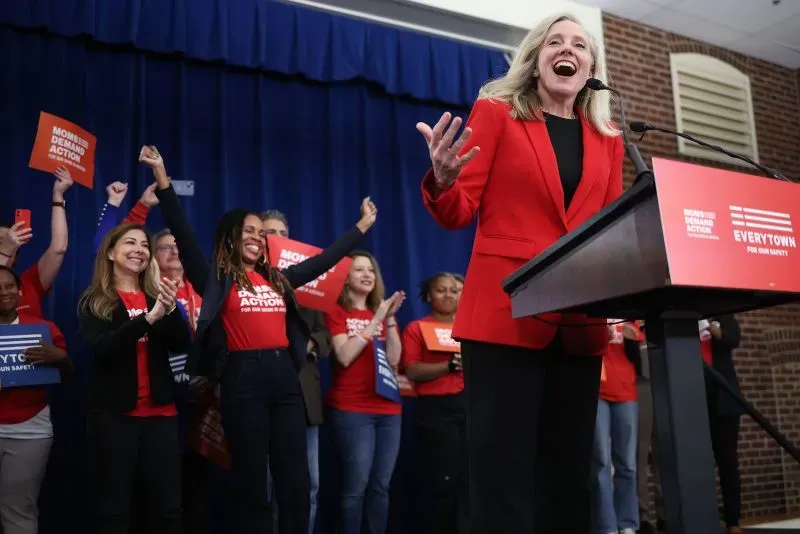 سبانبرغر تتحدث في فعالية انتخابية في نورفولك، محاطة بمؤيدين يرتدون قمصان حمراء، مع التركيز على خفض تكاليف الطاقة.