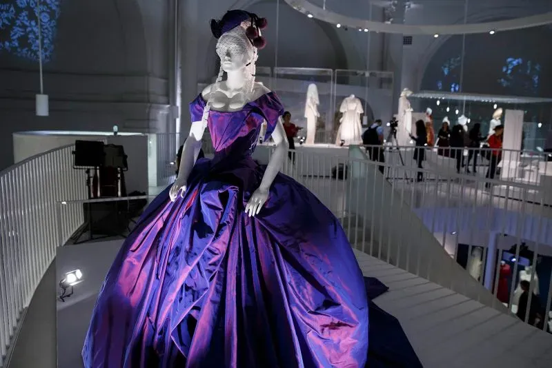 فستان زفاف بتصميم فيفيان ويستوود، يظهر بألوان جريئة وتفاصيل مميزة، مع خلفية لمعرض أزياء يعكس روح الابتكار في الموضة.