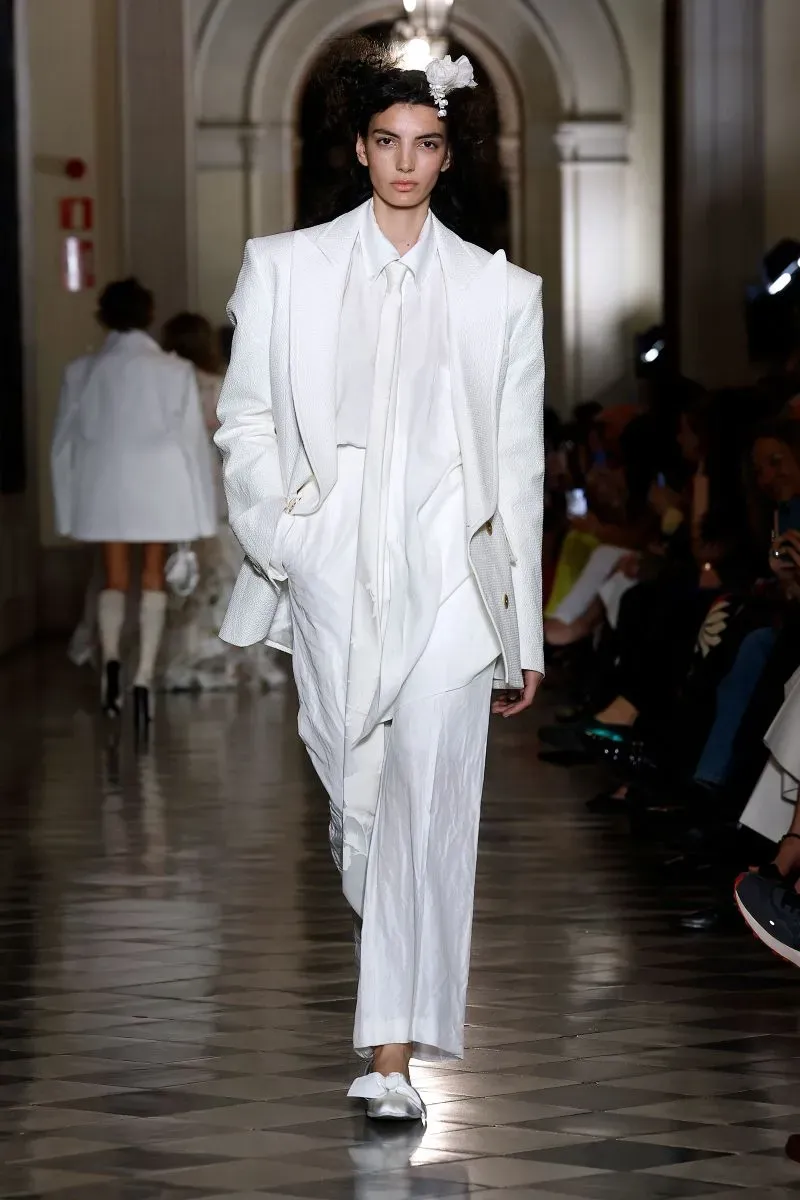 عارضة أزياء ترتدي بدلة زفاف بيضاء غير تقليدية من تصميم فيفيان ويستوود، تعرض في أسبوع الموضة للعرائس في برشلونة، مع تفاصيل مميزة.