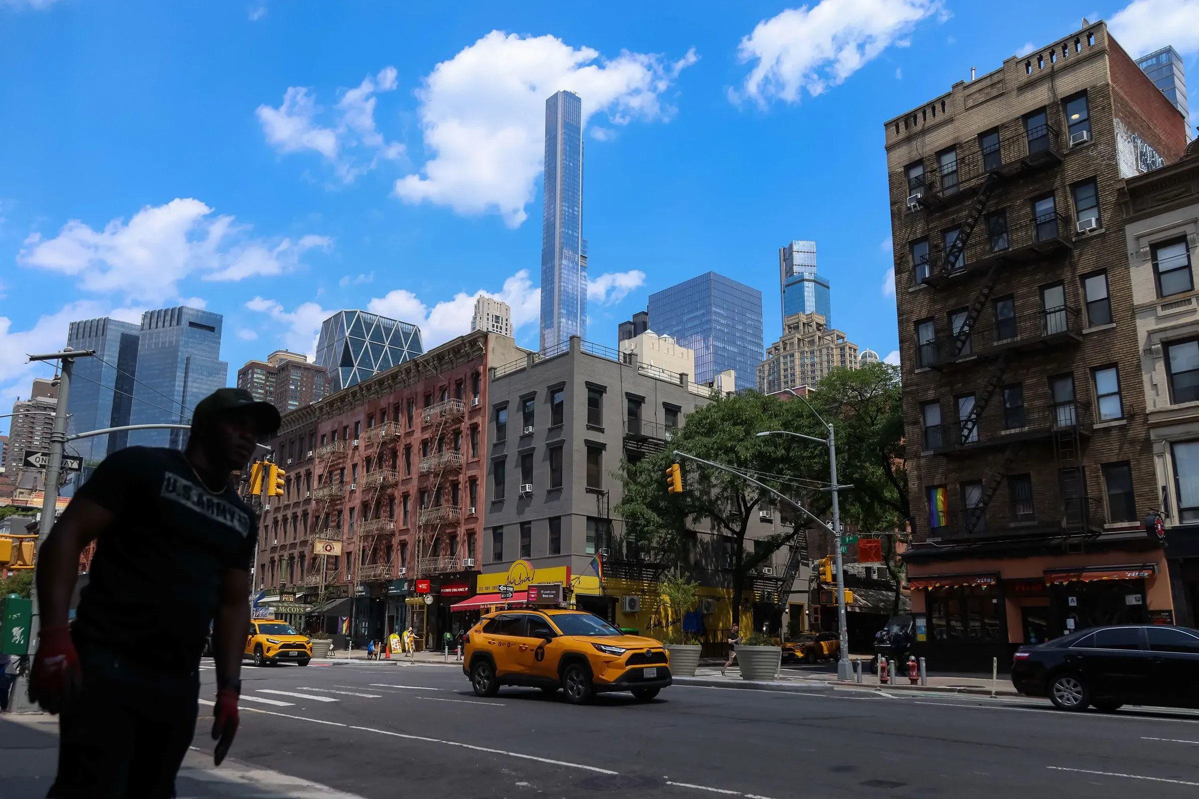 مشهد من مدينة نيويورك يظهر مباني تاريخية وحديثة، مع وجود سيارة أجرة أصفر وشخص يسير في الشارع، مما يعكس أزمة الإسكان الحالية.