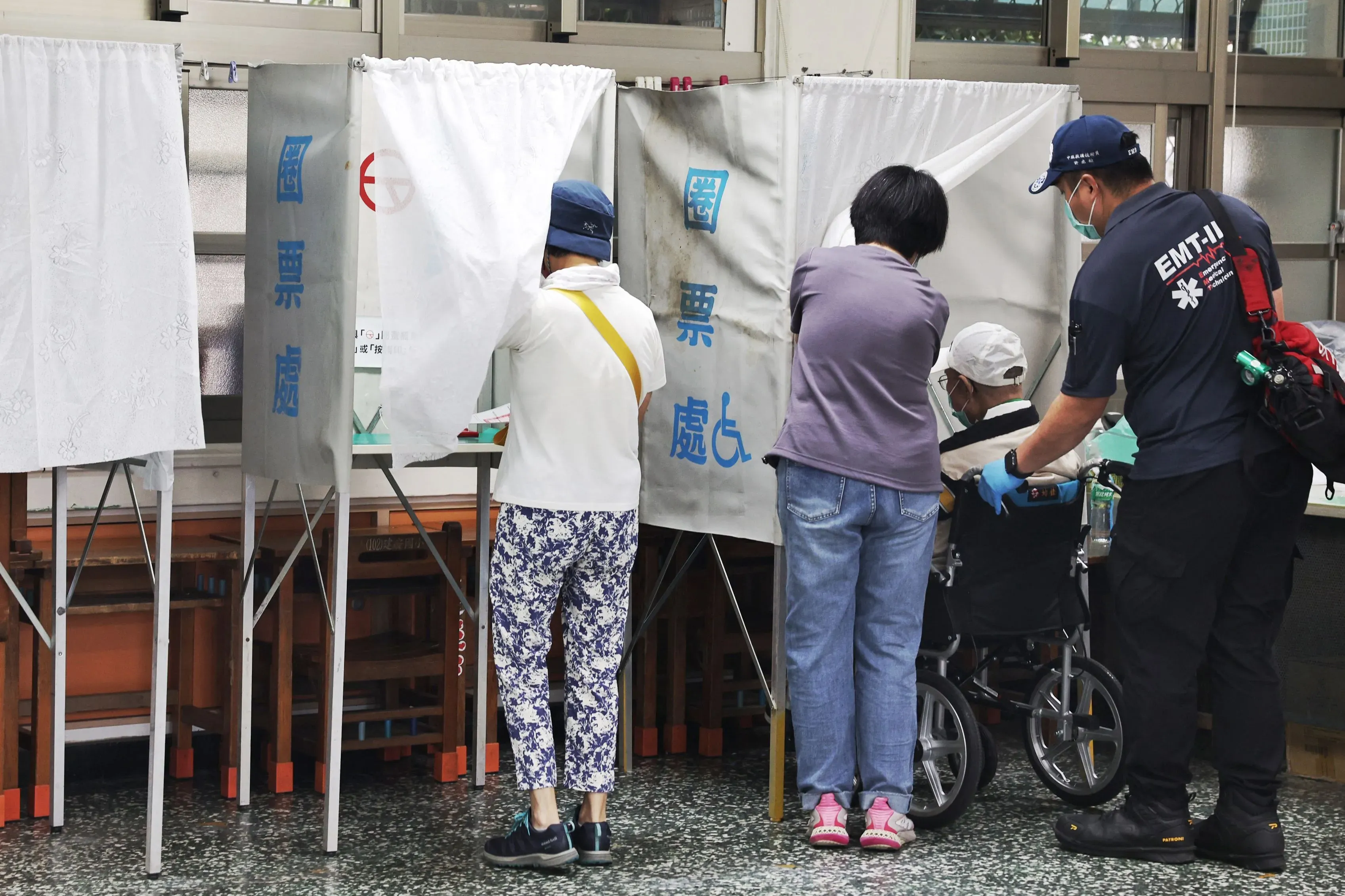 ناخبون في تايوان داخل مراكز الاقتراع خلال انتخابات سحب الثقة، مع وجود مسعف يساعد شخصًا مسنًا على كرسي متحرك.