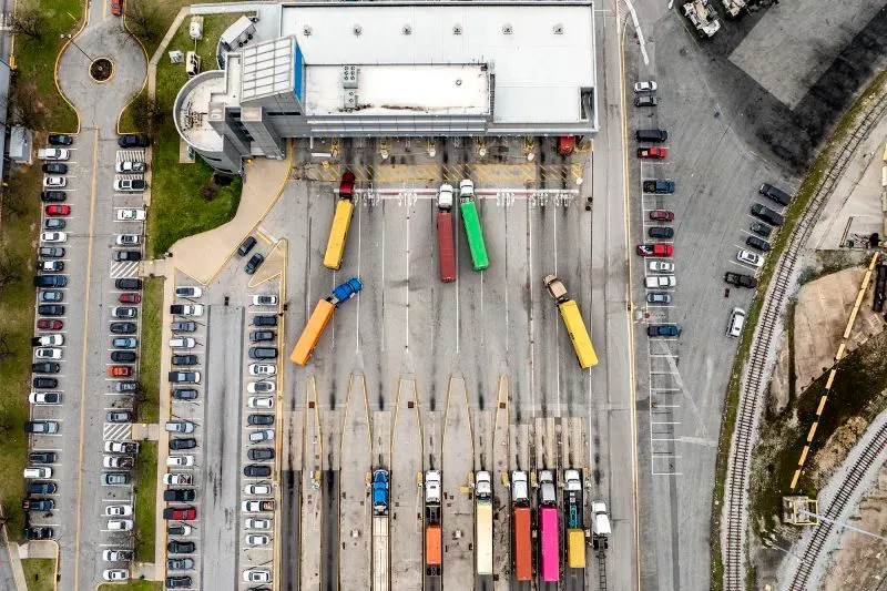 صورة جوية لمركز توزيع يحتوي على شاحنات ملونة متوقفة في صفوف، مع وجود سيارات في موقف السيارات المجاور.