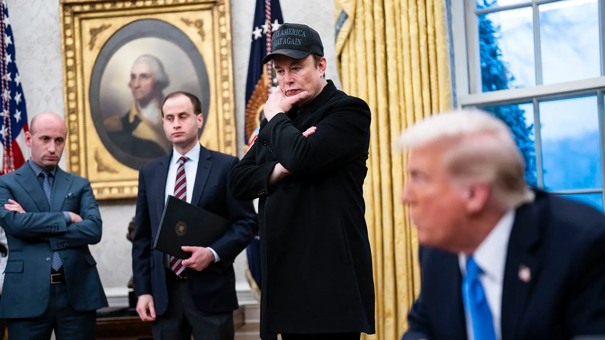 إيلون ماسك يظهر في المكتب البيضاوي مرتديًا قبعة تحمل عبارة "اجعل أمريكا عظيمة مرة أخرى"، بينما يبدو على وجهه التعبير الجاد.