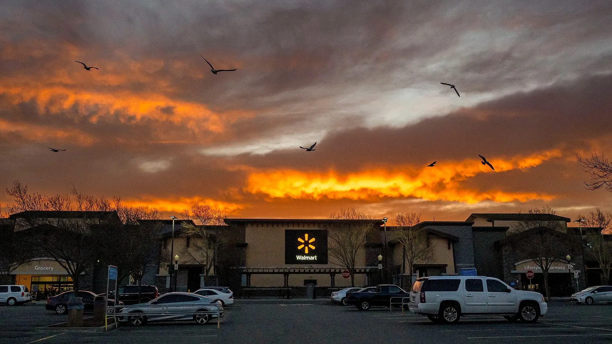 غروب الشمس خلف متجر وول مارت، مع طيور تحلق في السماء، مما يعكس حالة عدم اليقين في السوق وتأثير الرسوم الجمركية.