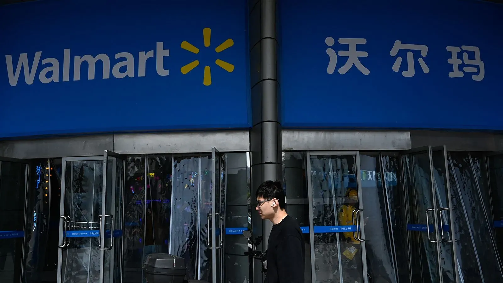 واجهة متجر وول مارت مع زبون يسير بجانب الأبواب الزجاجية، تعكس تأثيرات الحرب التجارية بين الولايات المتحدة والصين على سلاسل التوريد.