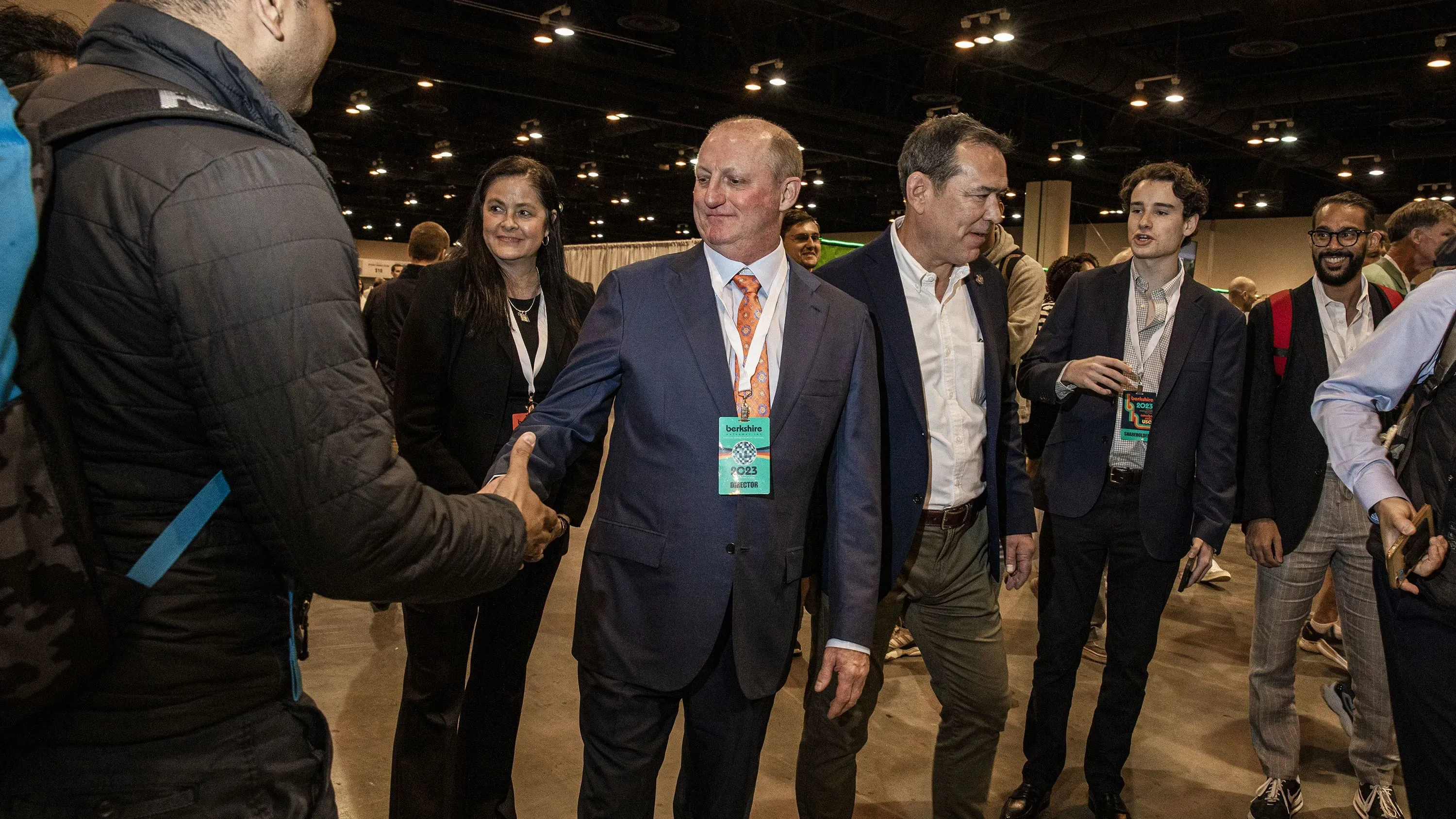 اجتماع للمساهمين في بيركشاير هاثاواي حيث يعلن وارين بافيت استقالته ويصافح جريج أبيل، المرشح لخلافته، وسط حضور عدد من المساهمين.