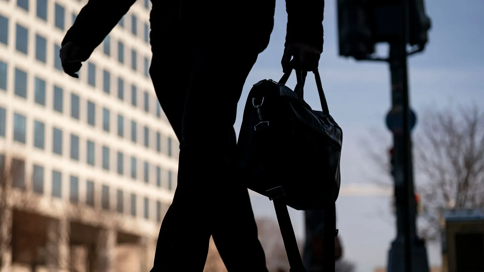 شخص يسير في الشارع حاملاً حقيبة، مع خلفية لمباني تجارية في واشنطن، يعكس تأثير تسريح العمال على الاقتصاد المحلي.