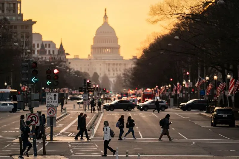 غروب الشمس فوق مبنى الكابيتول الأمريكي، مع مشاة يتنقلون في الشارع، مما يعكس التأثير الاقتصادي لفقدان الوظائف في العاصمة.