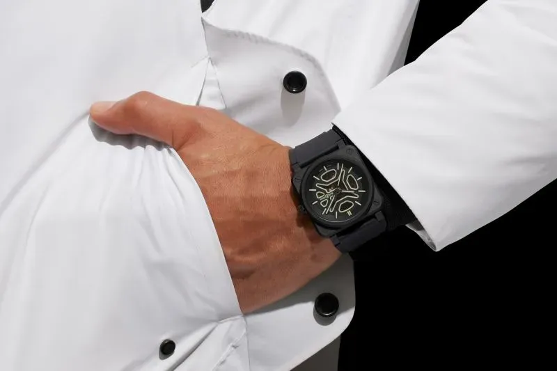 ساعة بيل آند روس BR 03 Skeleton مصممة بأسلوب رياضي مع تفاصيل أنيقة، تُظهر اليد مرتدية الساعة مع سترة بيضاء.