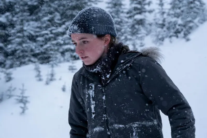 امرأة ترتدي قبعة سميكة ومعطفاً داكناً، تتعرض لتساقط الثلوج في بيئة جبلية، تعكس أجواء القلق والتوتر في مسلسل "The Last of Us".