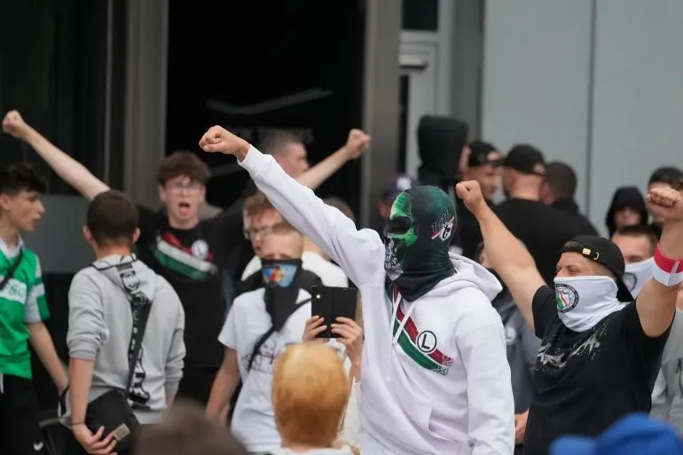 مجموعة من المتظاهرين في تورون، بولندا، يرفعون قبضاتهم أثناء مسيرة مناهضة للهجرة، مع لافتات تدعو لوقف الهجرة غير الشرعية.