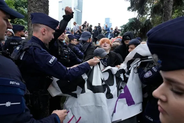 محتجون يرفعون لافتات خلال مسيرة في تورون، بولندا، بينما تتدخل الشرطة لتفريقهم وسط أجواء مشحونة ضد المهاجرين.