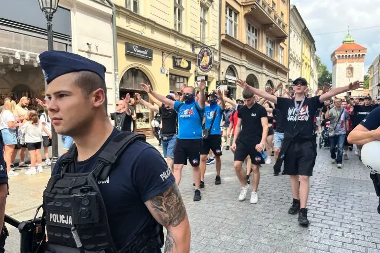 مسيرة احتجاجية في مدينة بولندية، حيث يحمل المتظاهرون لافتات ضد الهجرة، بينما يراقبهم أفراد الشرطة في الخلفية.