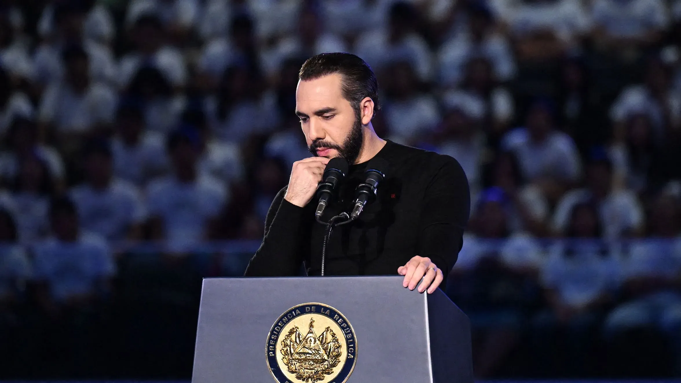 ناييب بوكيلي يتحدث في حدث رسمي، مع وجود شعار الحكومة خلفه، وسط جمهور كبير يرتدي ملابس بيضاء.