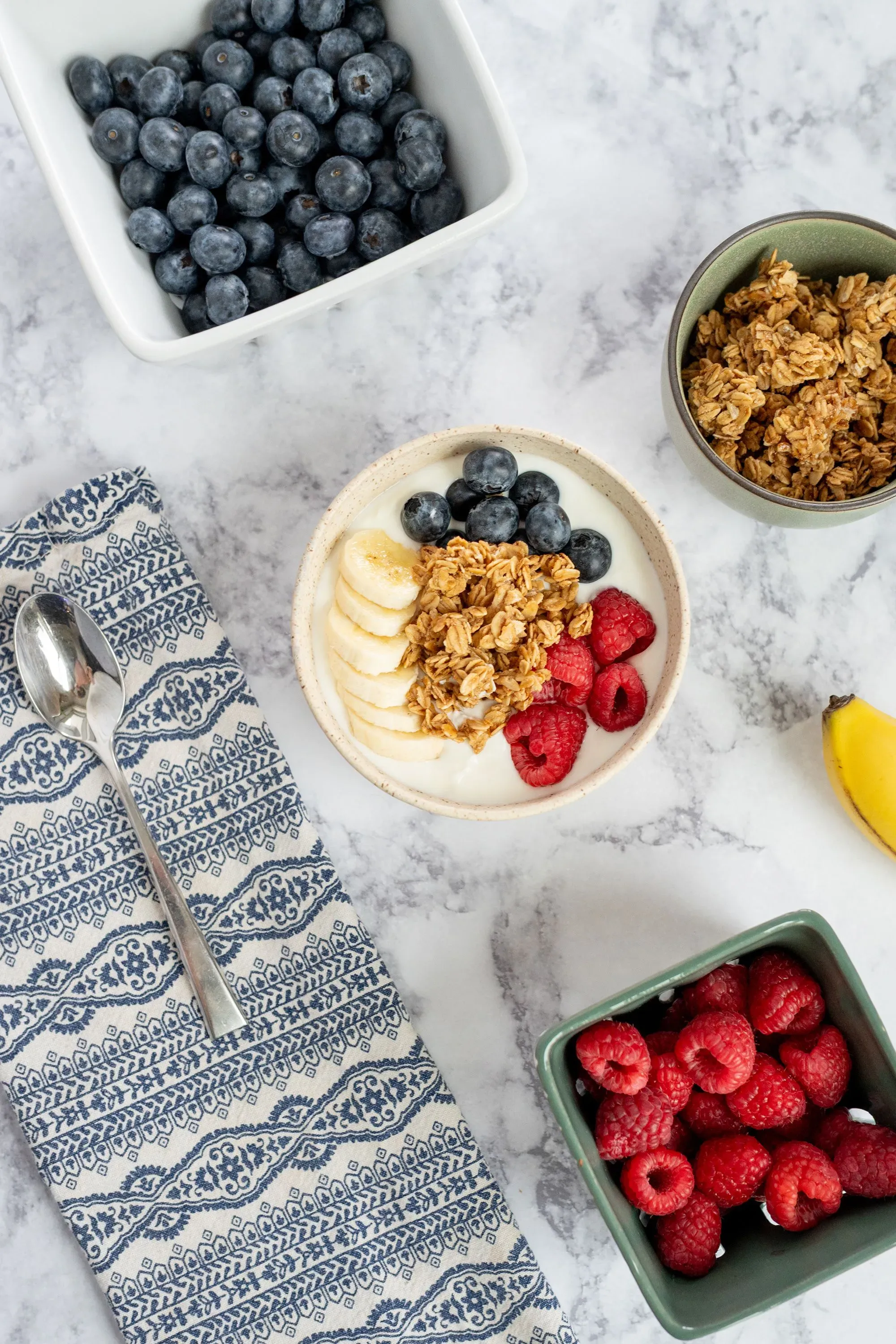 طبق يحتوي على زبادي مع جرانولا، توت أزرق، توت أحمر، وموز، مع فواكه طازجة، يعكس خيارات الإفطار الصحية وفقاً للإرشادات الغذائية الحديثة.