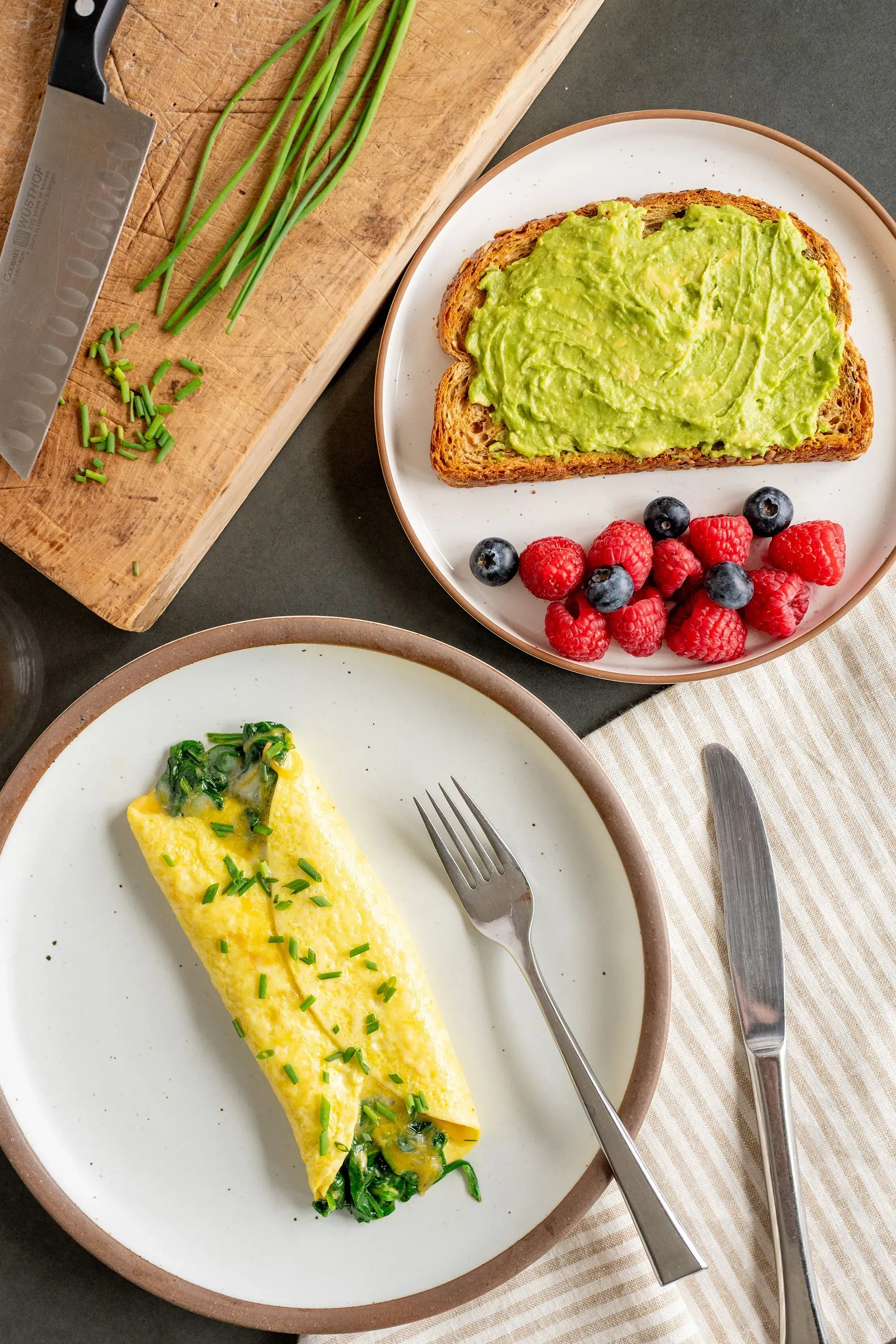 طبق إفطار صحي يتضمن أومليت بالسبانخ، توست بالأفوكادو، وتشكيلة من التوت، مما يعكس إرشادات التغذية الحديثة.