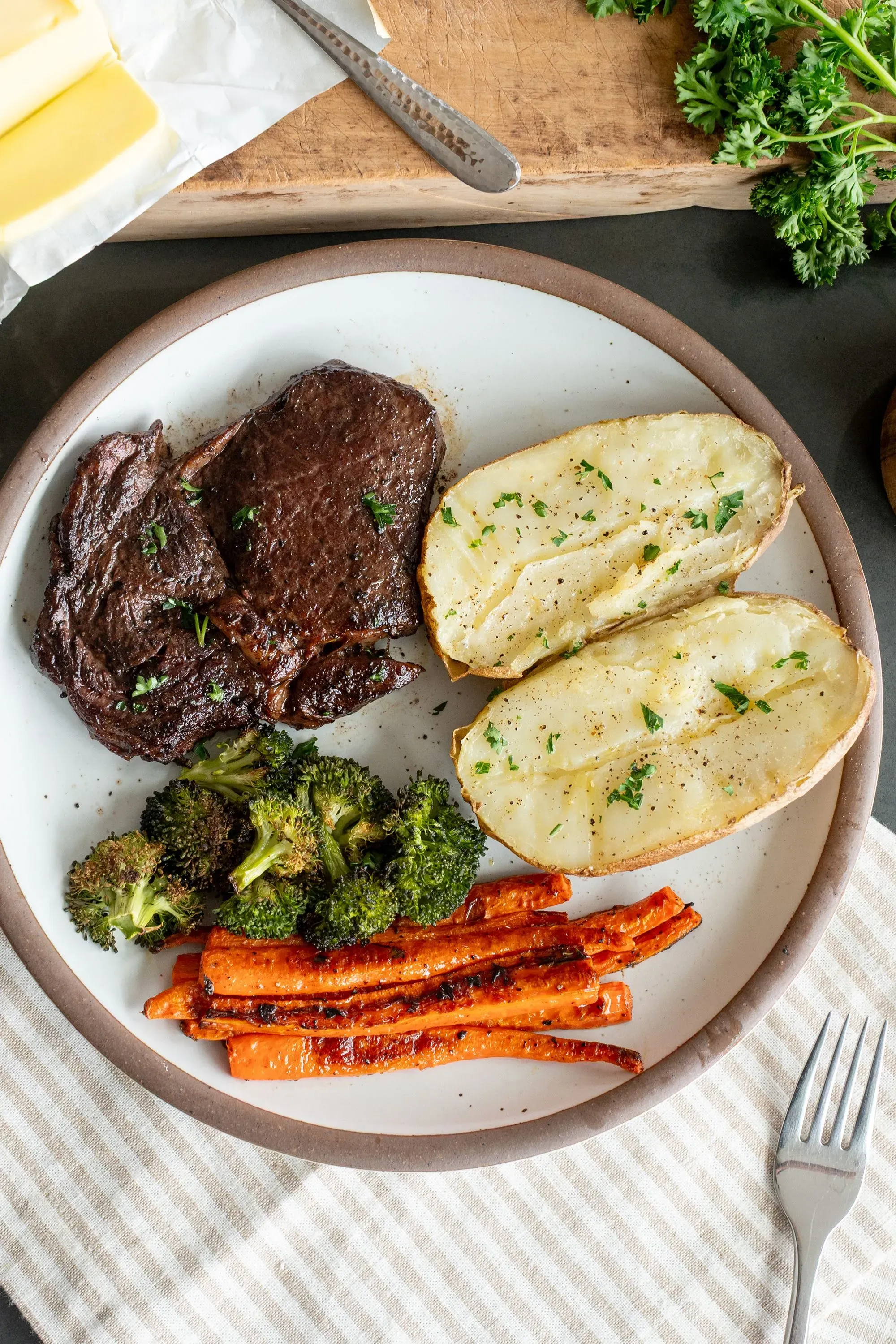 طبق يحتوي على شريحة لحم مشوية، بطاطا مشوية، بروكلي، وجزر مشوي، مع تزيين بالأعشاب. يمثل وجبة صحية تتماشى مع إرشادات التغذية الحديثة.