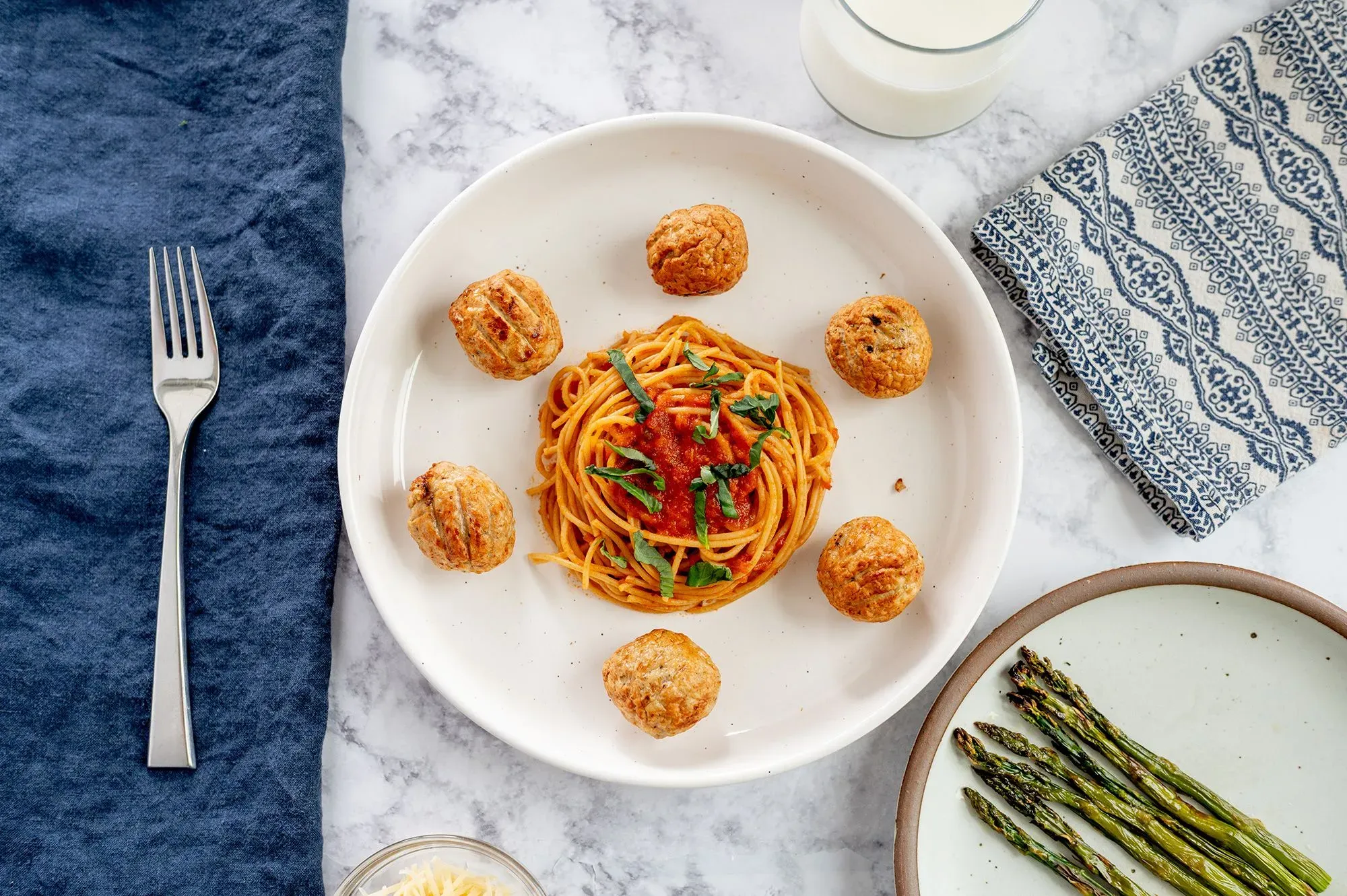 طبق مكون من المعكرونة مع صلصة الطماطم، كرات اللحم، وحبوب الهليون، بجانب كوب من الحليب، يعكس إرشادات الحمية الغذائية الحديثة.