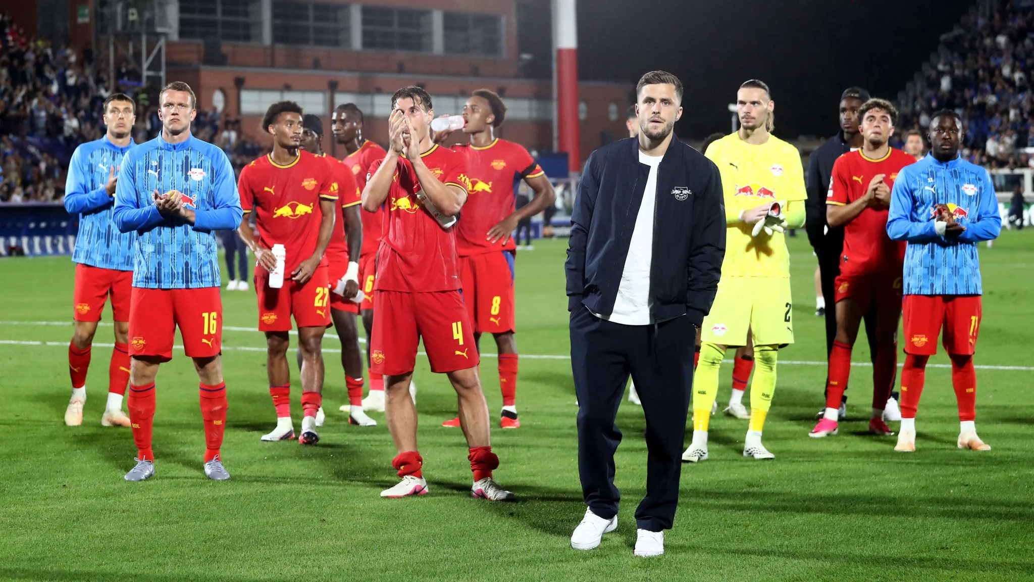 لاعبو فريق لايبزيغ يقفون على أرض الملعب بعد خسارتهم 4-1 أمام كومو في افتتاح دوري أبطال أوروبا، مع تعابير خيبة أمل واضحة.