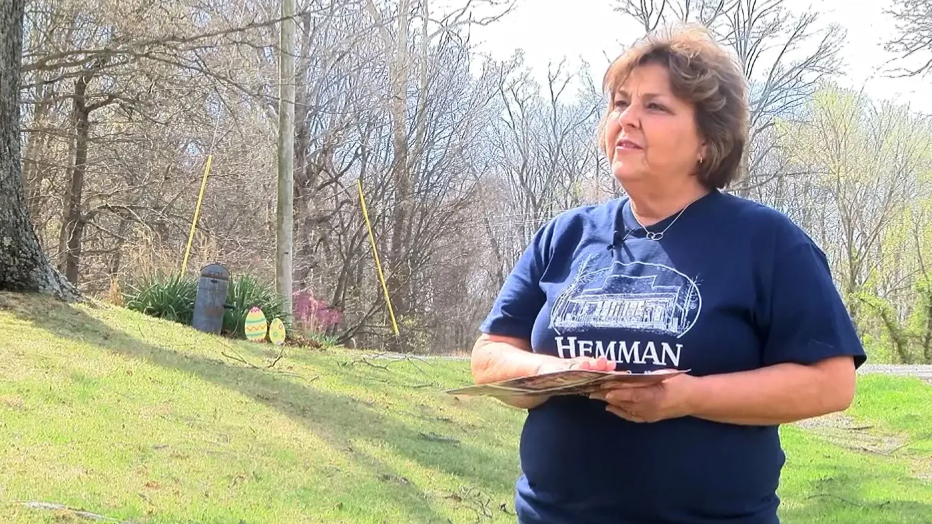 امرأة تحمل صورًا في يديها، تقف في فناء منزلها بعد إعصار EF3 في بوبلار بلاف، ميسوري، تعبر عن امتنانها للمساعدة المجتمعية.