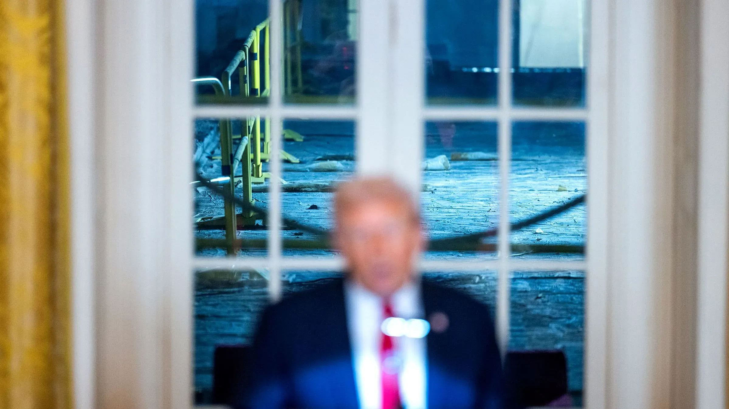 اجتماع أسبوعي في البيت الأبيض حيث يظهر ترامب أمام نافذة، مع مشهد لأعمال تجديد في الخلفية تشمل حواجز وأرضية غير مكتملة.