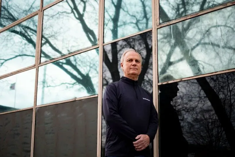 رجل الأعمال غرايم روستان يقف أمام نافذة زجاجية تعكس الأشجار، معبرًا عن مخاوفه من تأثير الحرب التجارية على صناعة الهوكي.