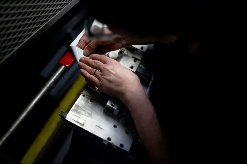 يدًا رجل يعمل على تصنيع عصا هوكي، مع التركيز على تفاصيل الآلة المستخدمة، في سياق تأثير الحرب التجارية على الصناعة.