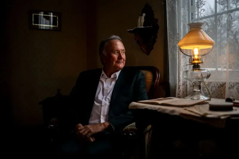 رجل الأعمال غرايم روستان يجلس في غرفة مضاءة بمصباح تقليدي، معبرًا عن قلقه بشأن تأثير الحرب التجارية على أعماله في كندا.