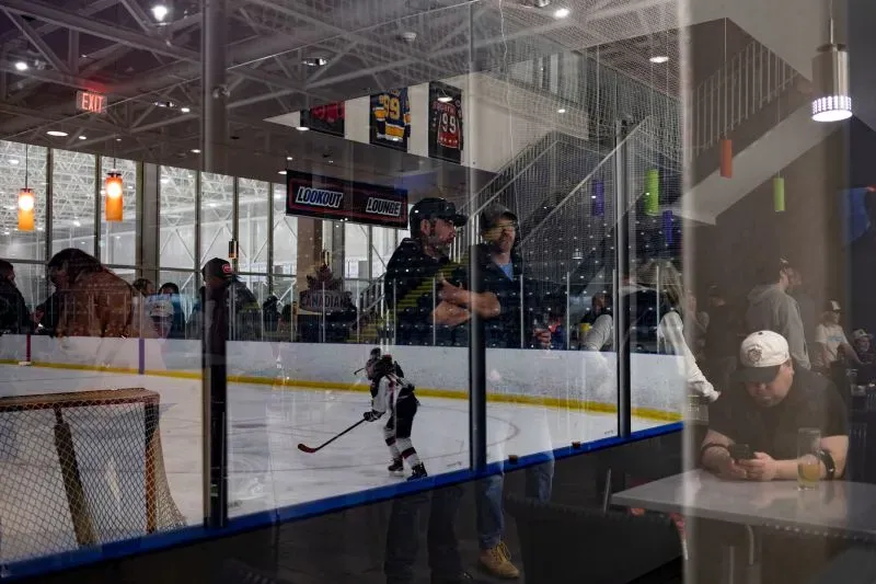 مشهد داخلي لمركز رياضي حيث يتجمع المشجعون لمشاهدة مباراة هوكي، مع لاعب صغير يتزلج على الجليد في الخلفية.